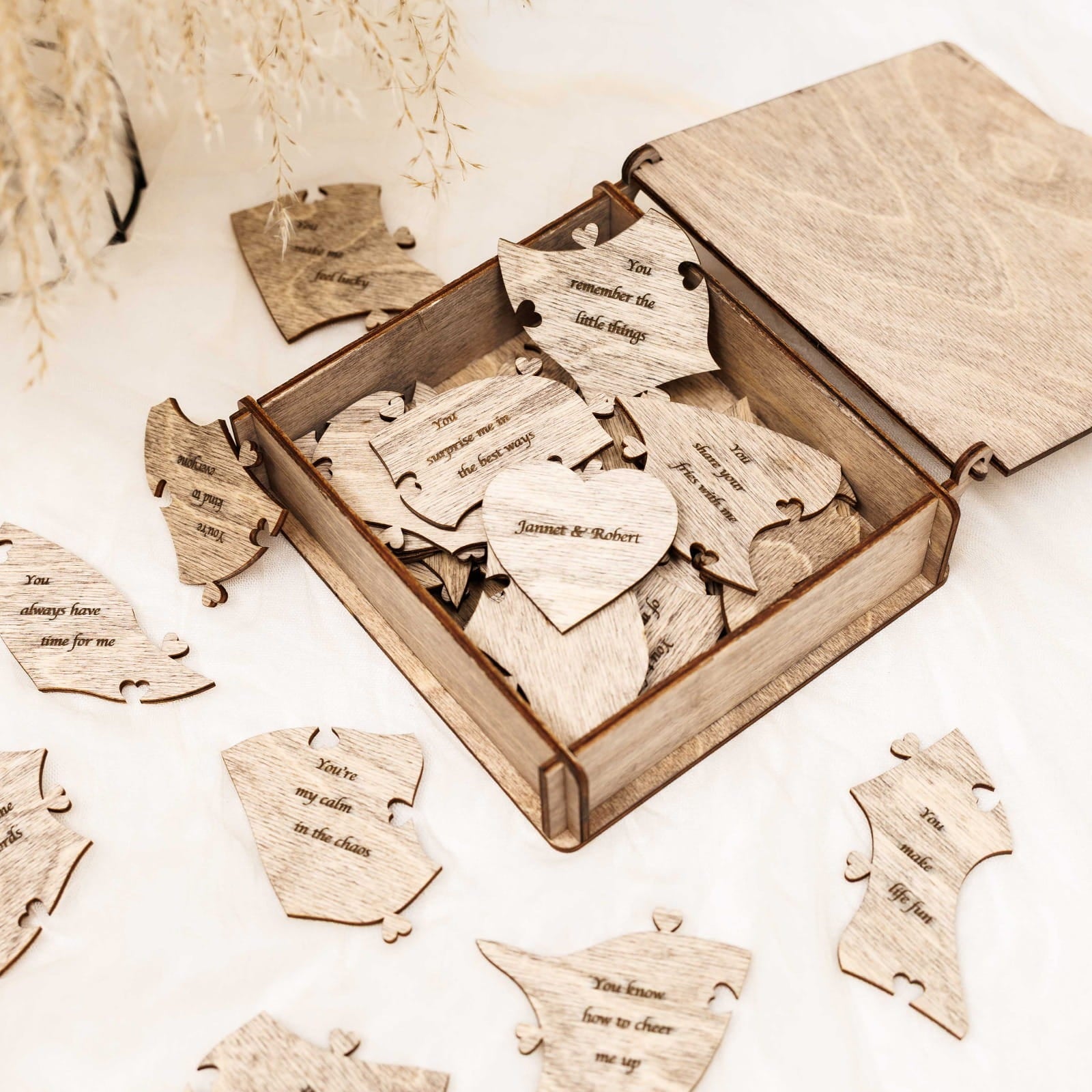 Wooden heart-shaped puzzle pieces with engraved text in an open wooden box.