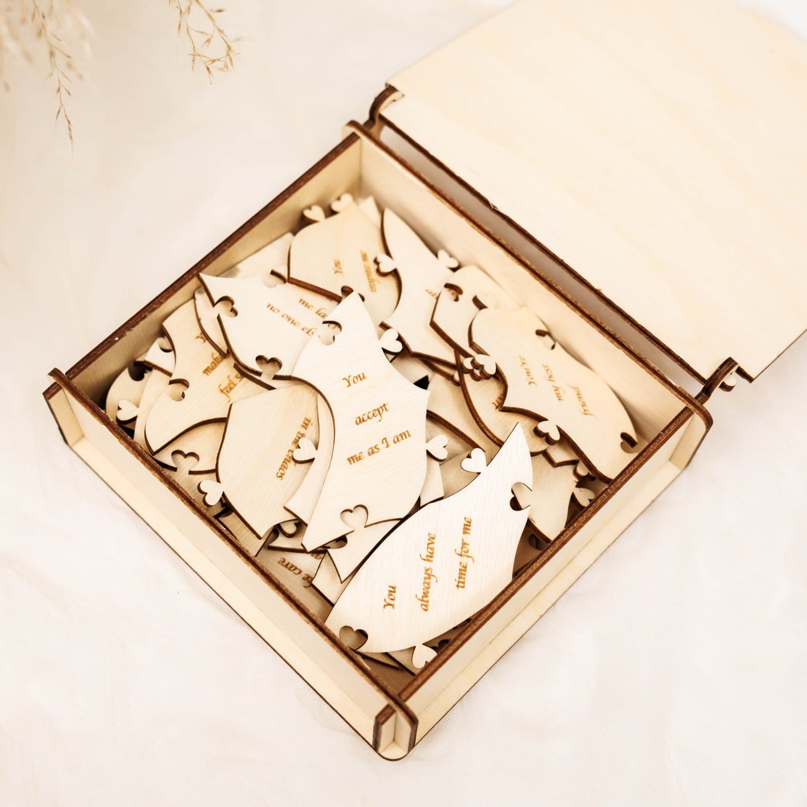 Wooden heart-shaped puzzle pieces with engraved text in an open box on a light background