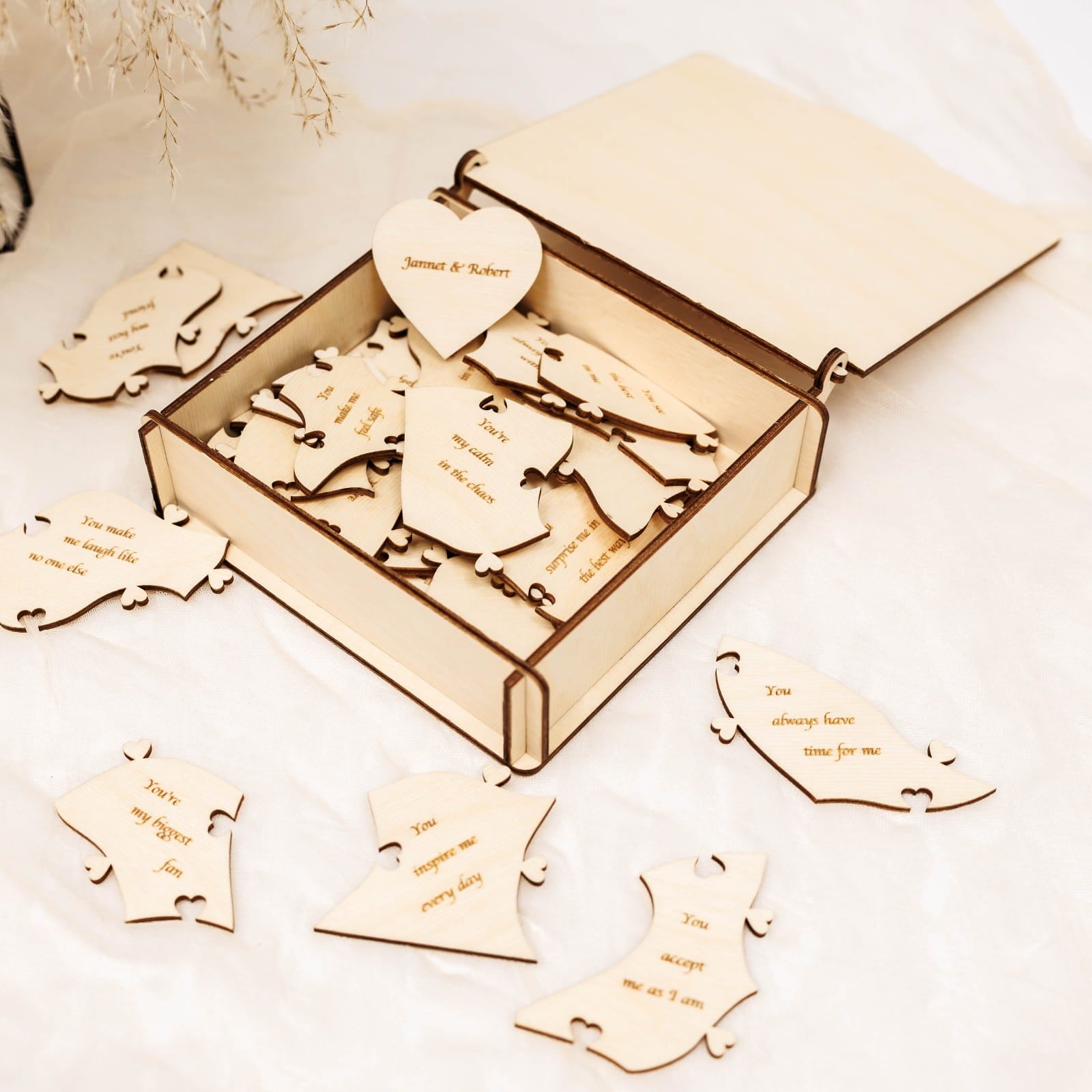 Wooden heart-shaped puzzle pieces with engraved text in an open box on a light background