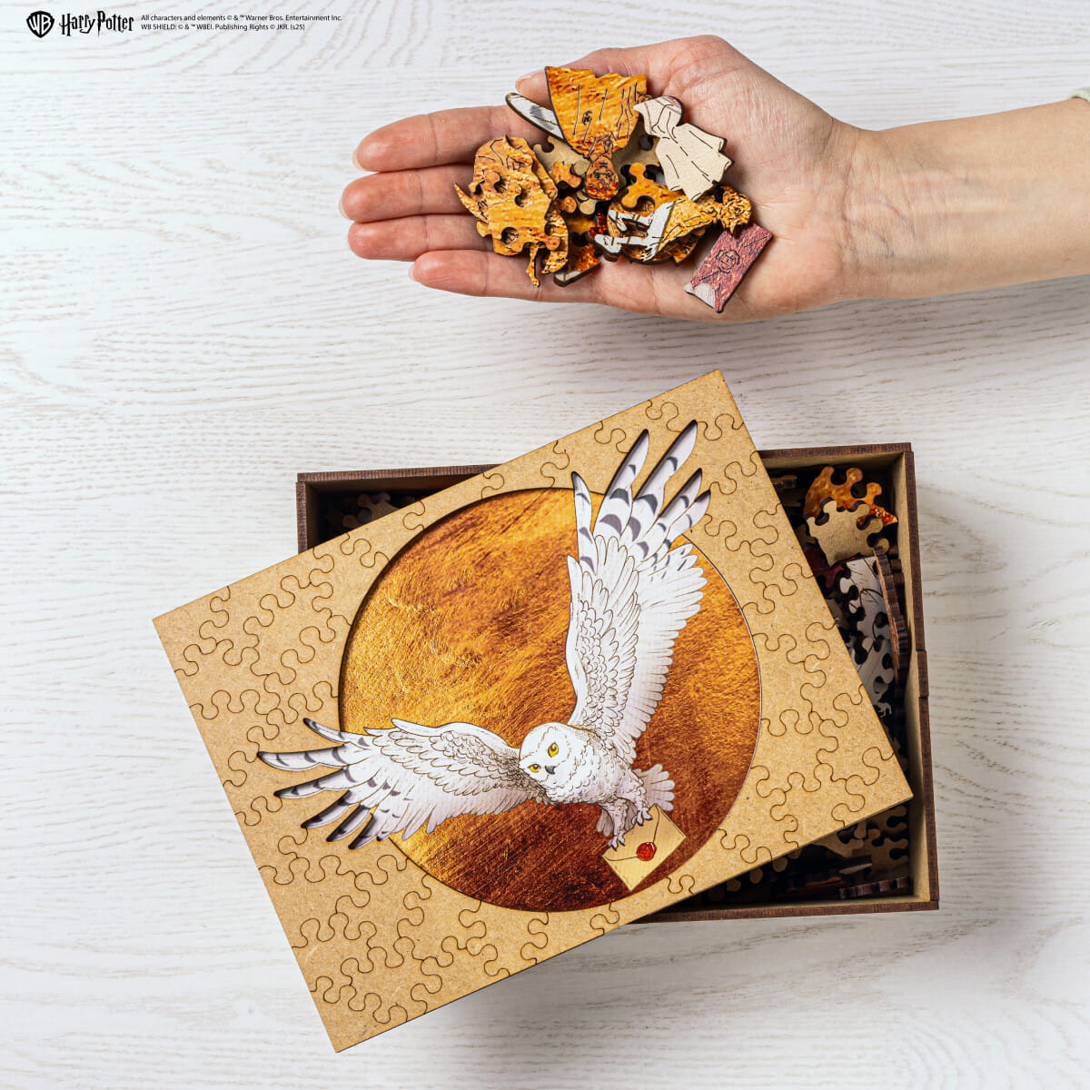 Hand holding puzzle pieces with a partially completed puzzle featuring an owl on a wooden box.