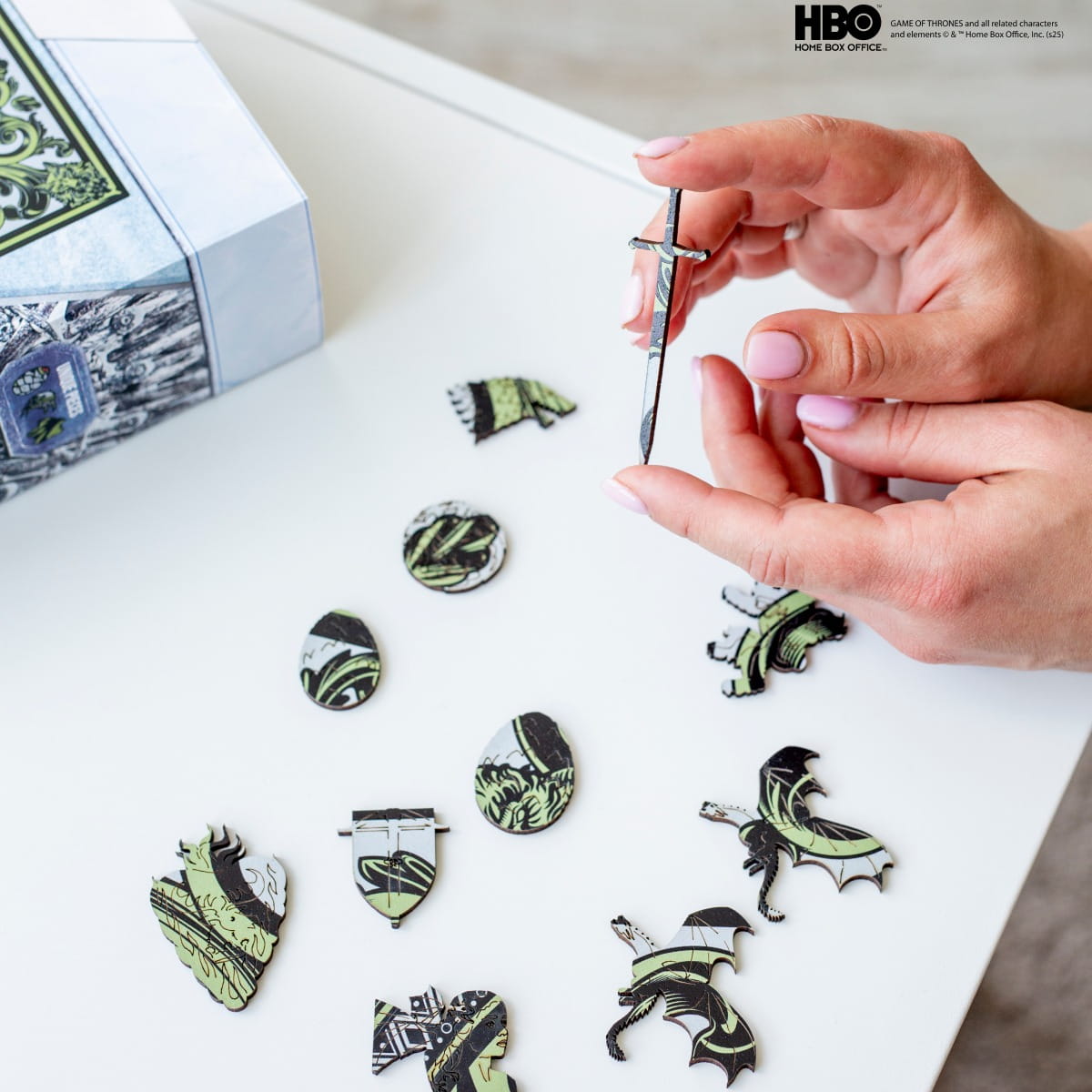 Person assembling decorative pieces with a Game of Thrones theme on a white surface.
