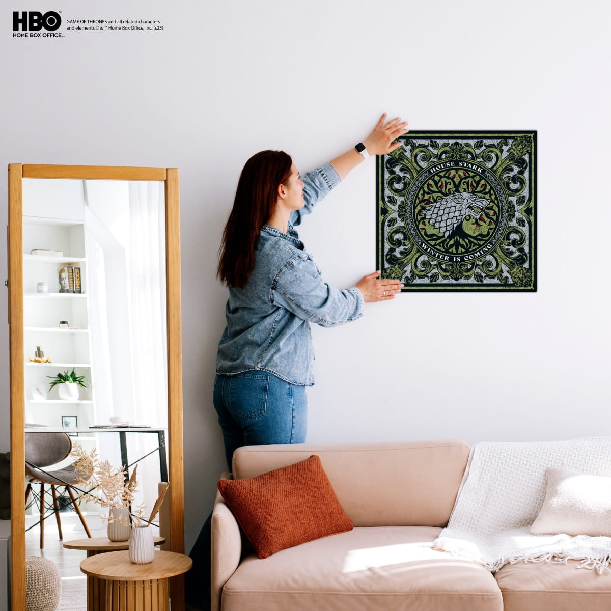Woman hanging a framed artwork on a wall in a living room.