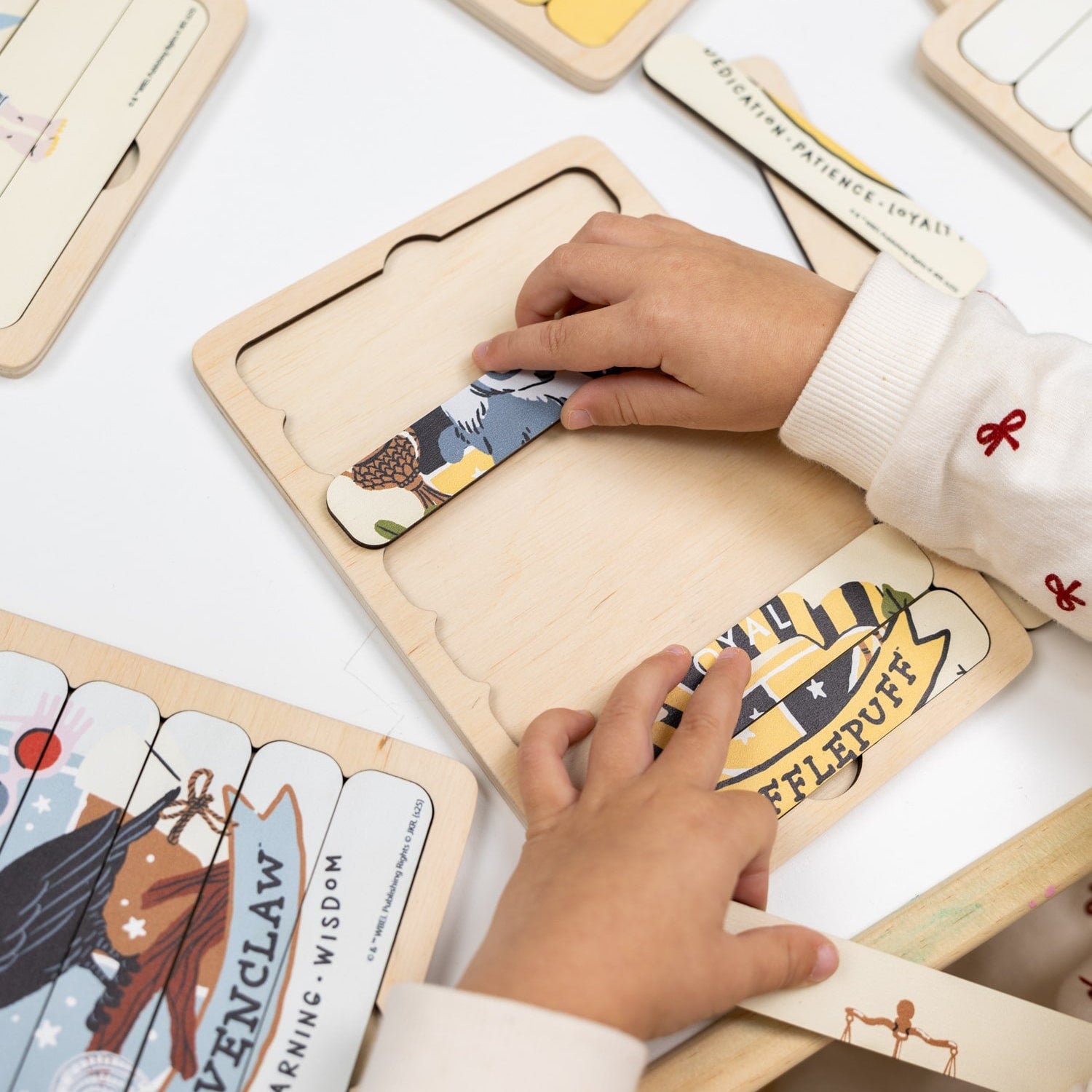 Children's hands interacting with wooden cards featuring Harry Potter designs on a white surface.