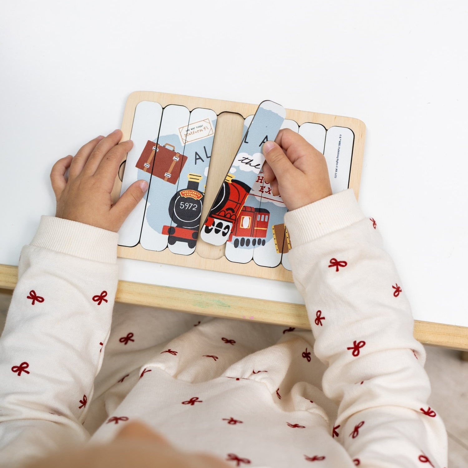 Child playing with a wooden puzzle featuring train designs on a white background