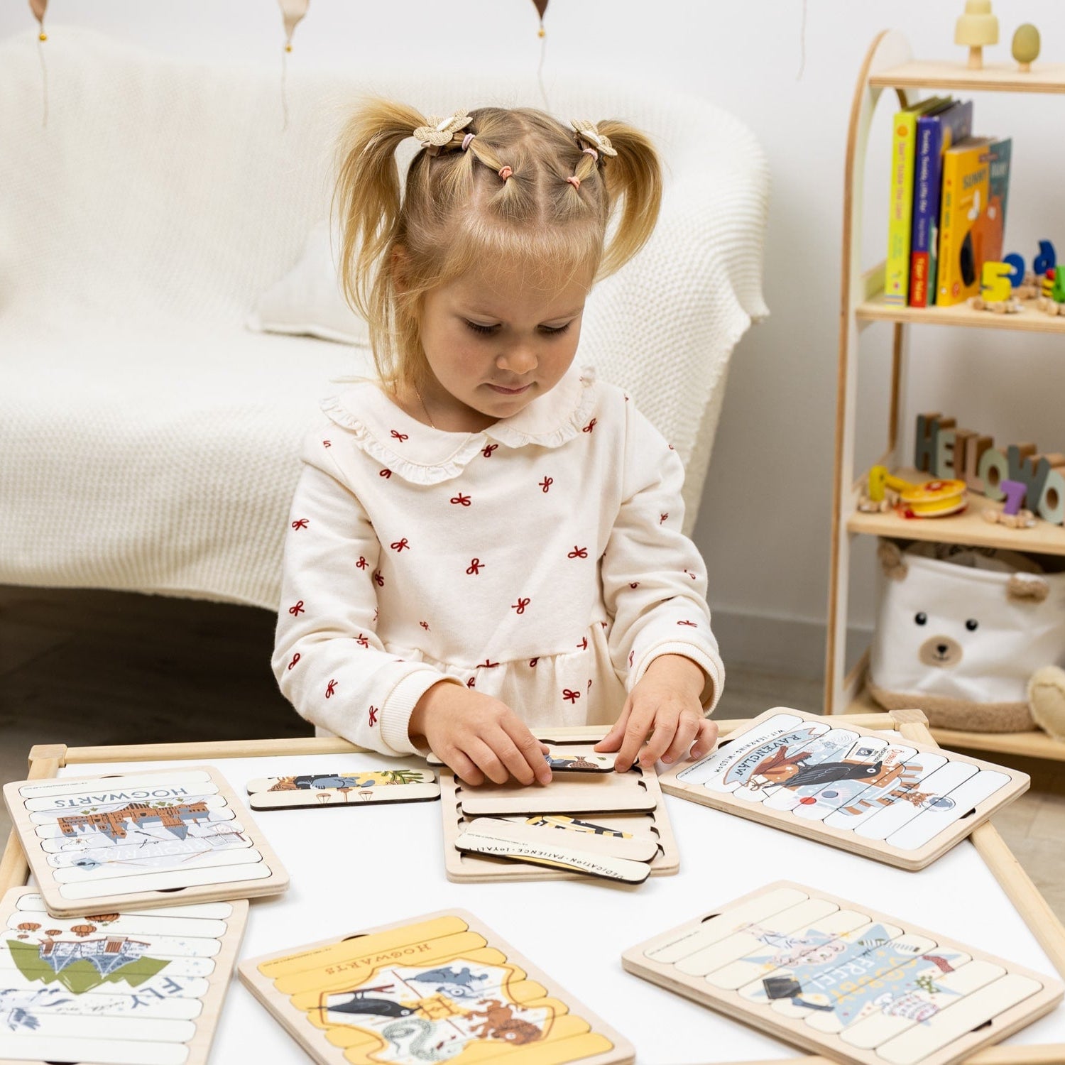 Young girl playing with educational toys on a table in a room with a shelf of books and toys.