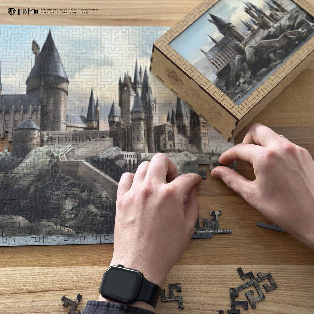 Person assembling a puzzle of Hogwarts castle with a completed puzzle in the background.