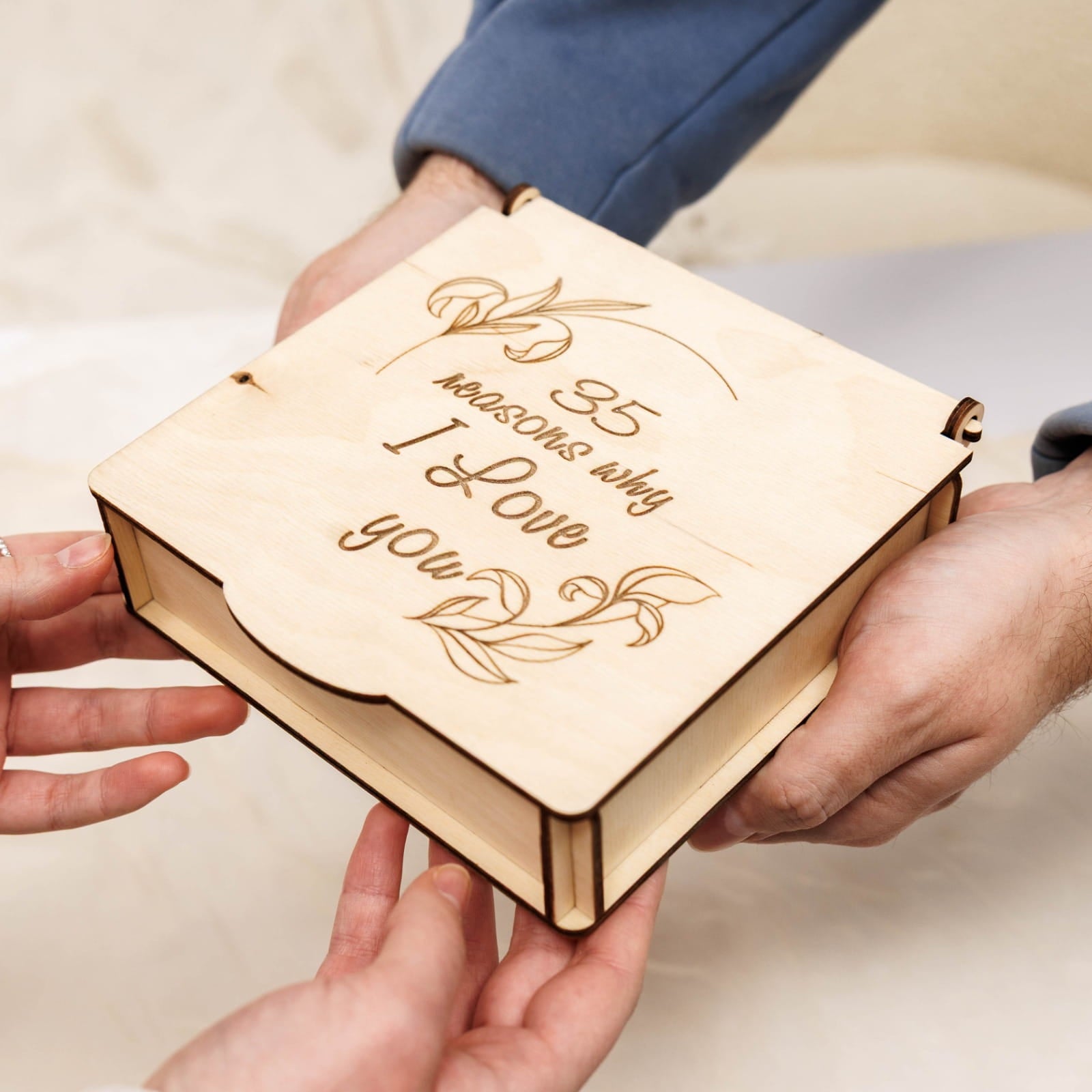 Wooden box with '35 reasons why I love you' engraving held by hands.