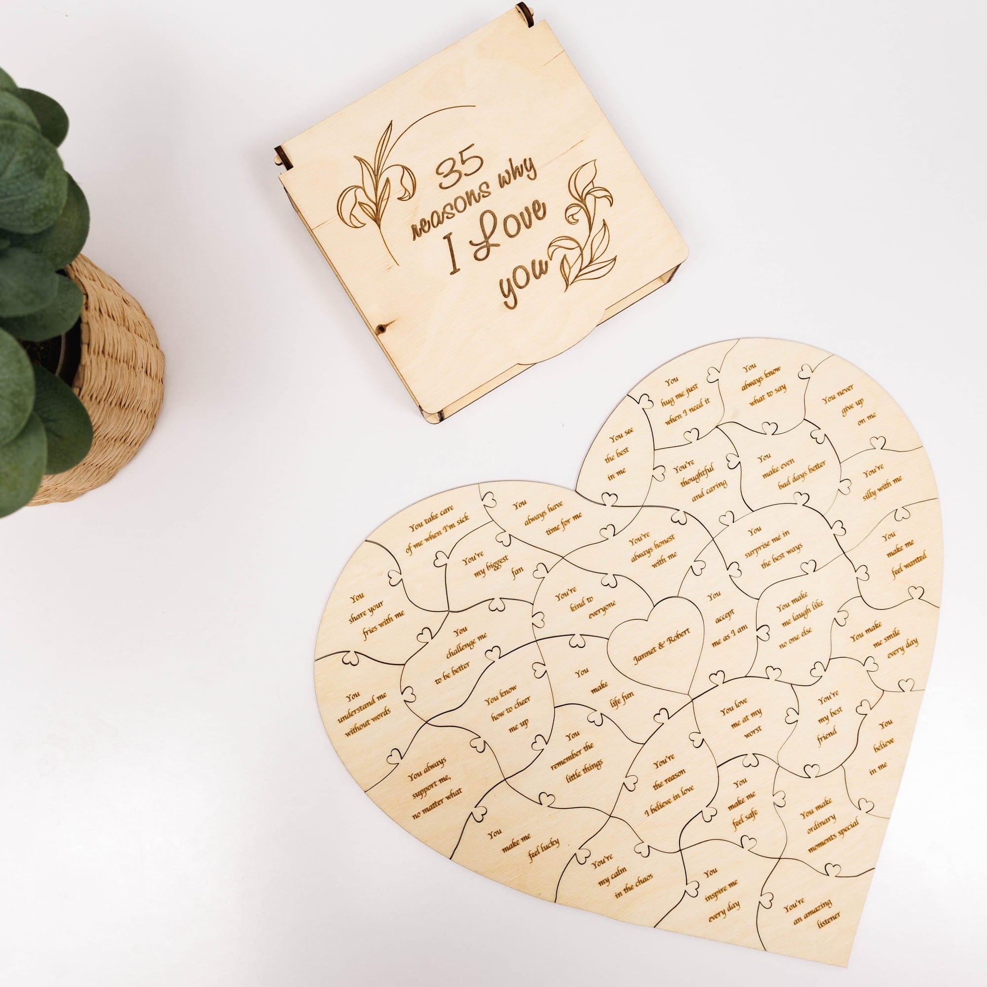 Heart-shaped wooden puzzle with engraved text on a white surface with a plant in the corner.
