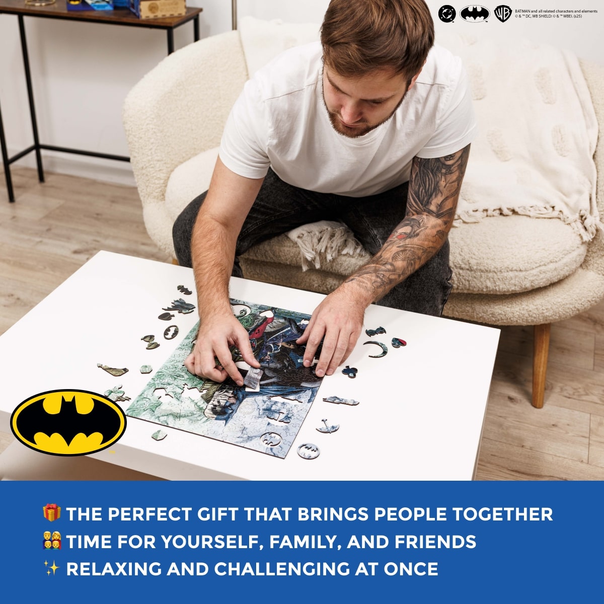 Man sitting on a couch working on a Batman-themed puzzle with a Batman logo in the corner.