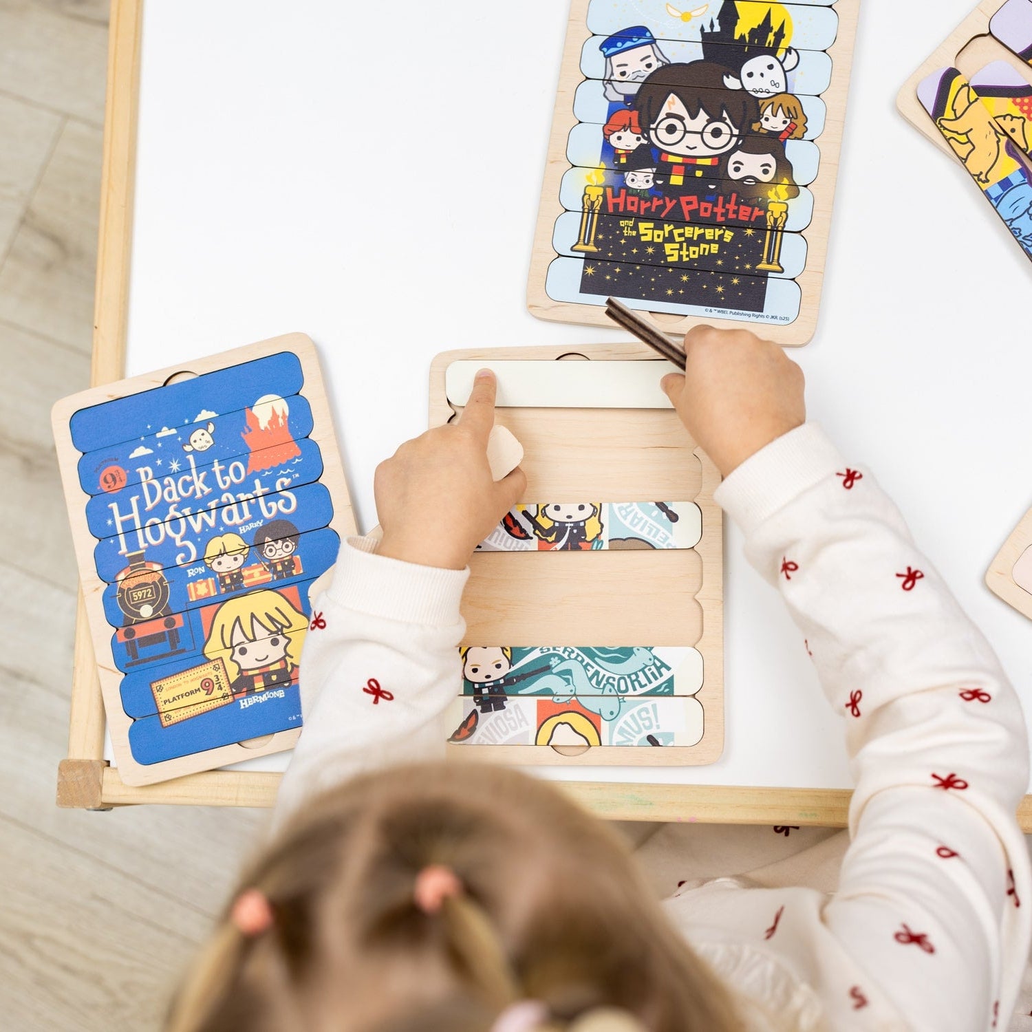 Child playing with Harry Potter-themed wooden puzzle on a light wooden floor.