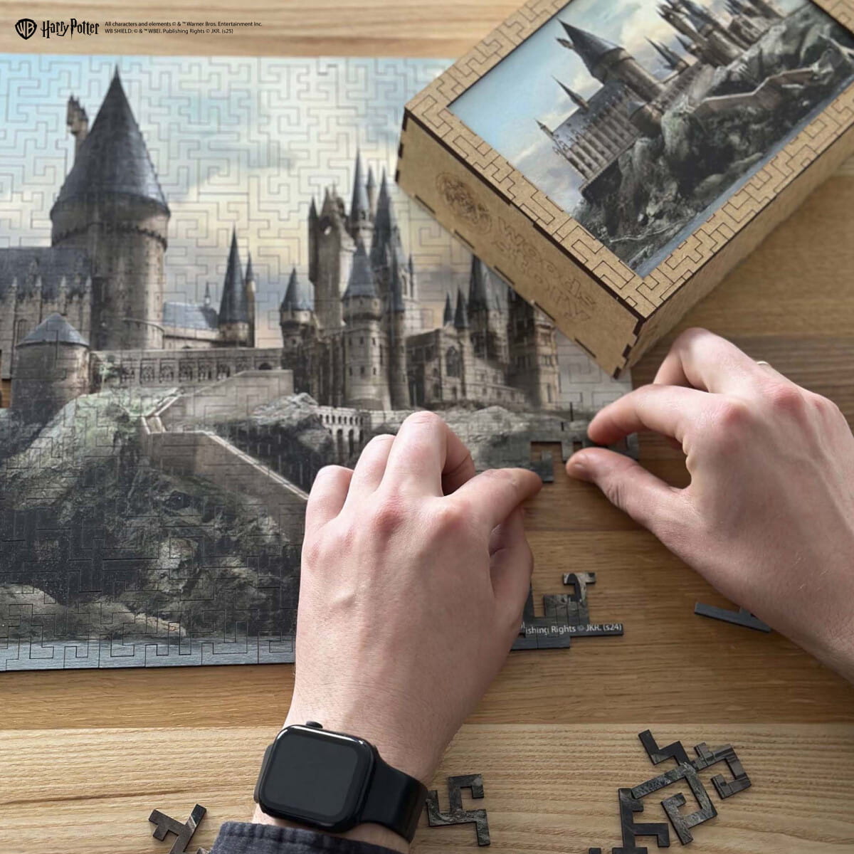 Person assembling a puzzle of Hogwarts castle from Harry Potter on a wooden table.